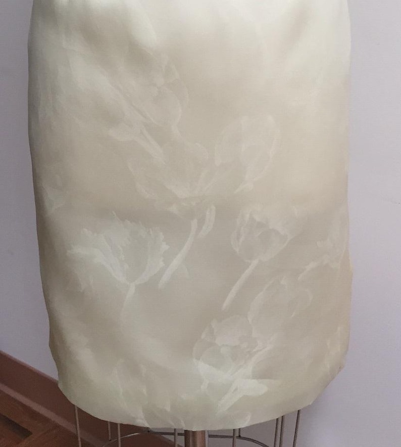 Puede incluir: Una falda blanca con un sutil estampado floral en relieve. La falda est&aacute; hecha de una tela ligera y tiene una textura suave y sedosa.