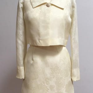May include: A vintage ivory-colored dress suit with a cropped jacket and a skirt. The fabric has a floral pattern.