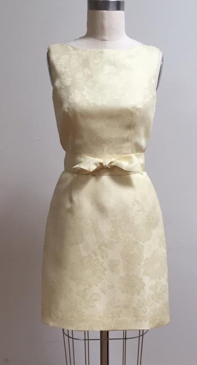 May include: A sleeveless, ivory dress with a floral pattern and a matching sash tied at the waist.