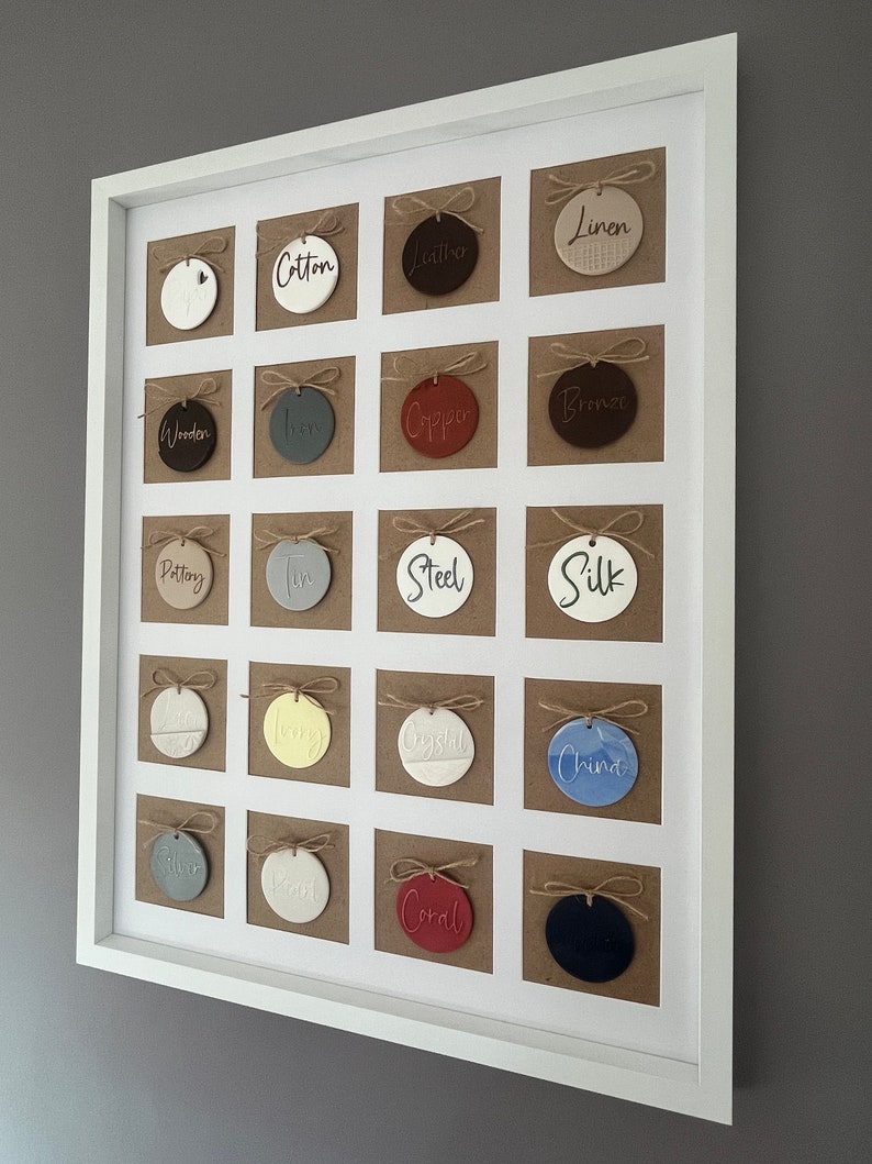 May include: A white frame with 20 round ceramic ornaments, each with a different color and word printed on it. The words include "Cotton", "Leather", "Linen", "Wooden", "Iron", "Copper", "Bronze", "Pottery", "Tin", "Steel", "Silk", "Silver", "Wool", "Crystal", "China", "Coral", "Black", "Gold", "White", and "Grey".