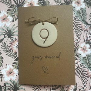 May include: A brown card with a white ceramic ornament attached with twine. The ornament has the number 9 on it. The card says "9 years married" with a heart symbol.