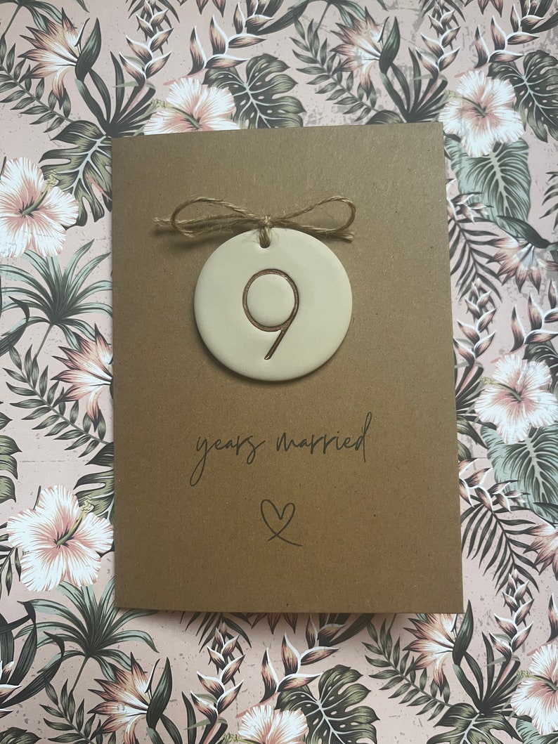 May include: A brown card with a white ceramic ornament attached with twine. The ornament has the number 9 on it. The card says "9 years married" with a heart symbol.