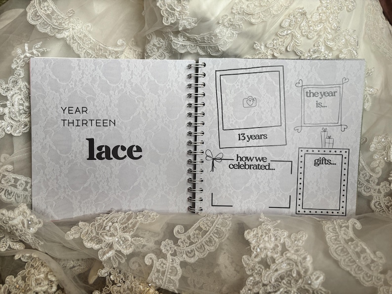 May include: A spiral-bound anniversary scrapbook with a white lace-patterned background. The left page reads YEAR THIRTEEN lace. The right page features hand-drawn frames for photos and text, including labels for 13 years, the year is, how we celebrated, and gifts.