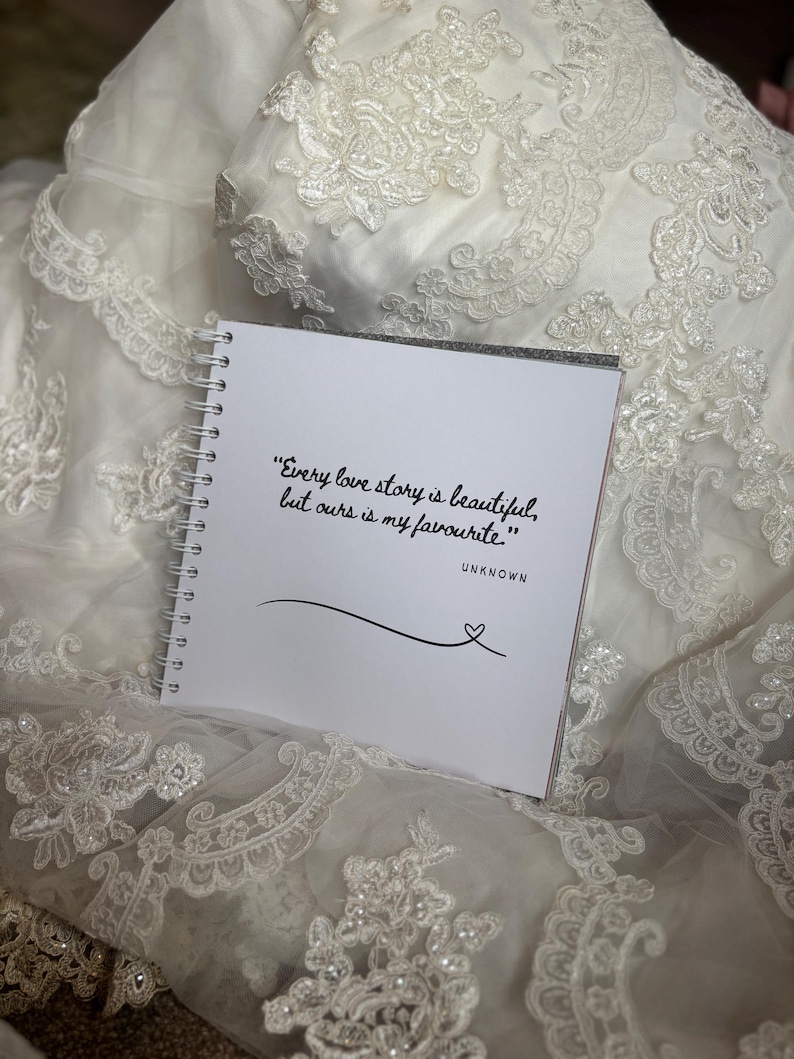 May include: A square white spiral-bound notebook featuring the black printed text, "Every love story is beautiful, but ours is my favourite." followed by the word "UNKNOWN" and a simple line drawing of a heart at the end of a curved line.