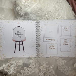 May include: A spiral-bound wedding scrapbook with white pages featuring gold star accents. The left page shows an easel illustration with the text Our Wedding Day. The right page contains outlined boxes for photos and notes labelled the big day, the date, our first dance, and cake flavour.