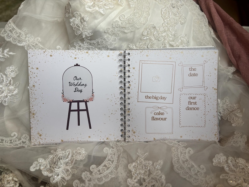 May include: A spiral-bound wedding scrapbook with white pages featuring gold star accents. The left page shows an easel illustration with the text Our Wedding Day. The right page contains outlined boxes for photos and notes labelled the big day, the date, our first dance, and cake flavour.