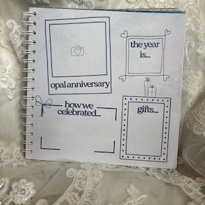 May include: A square spiral-bound scrapbook page with dark blue line art. It features a photo frame with a camera icon labelled opal anniversary, a box labelled the year is, a section labelled how we celebrated, and a box labelled gifts.