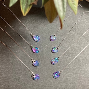 May include: A set of six pairs of dangle earrings with silver chains and iridescent resin charms in the shapes of teardrops and hearts. The charms have a mix of blue, purple, and green colours.