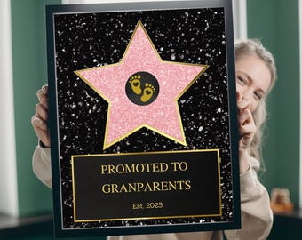 Puede incluir: Un letrero enmarcado con fondo negro y una estrella rosa brillante. La estrella tiene un contorno dorado y un diseño de huellas doradas en el centro. El letrero dice "PROMOTED TO GRANDPARENTS" y "Est. 2025".
