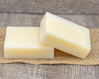 May include: Two bars of white soap on a brown burlap surface. The soap is rectangular and has a smooth, matte finish.