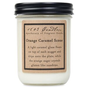 May include: A glass jar candle with a black lid. The label reads "1803 Candles" and "Orange Caramel Scone." The label describes the candle's scent with a caramel glaze and orange sugar crystals.