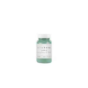 May include: A small, round, green paint jar with a white lid. The label reads "Alchemy, A blend of limestone & Chalk". The paint is a muted green color, and the jar is sitting on a white background.