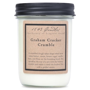 May include: A glass jar candle with a brown label that reads "1803 Candles Apothecary of Fragrant Goods Graham Cracker Crumble". The label also includes a description of the scent: "A crumbled dough takes shape when mom mixes butter, cream, brown sugar, vanilla bean, and flour on the kneading board. She sprinkles the top of a pie with the buttery crumble and bakes it until the kitchen fills with a golden aroma."