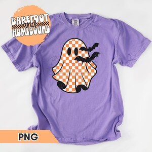 以下が含まれることがあります： 紫色のTシャツに、オレンジと白のチェック柄の白い幽霊と、その周りを飛ぶ黒いコウモリが描かれています。画像の左上隅には「Barefoot and Homebound」というテキストがあります。