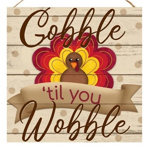 May include: A wooden sign with a white background and brown polka dots. The sign features a cartoon turkey with a red, yellow, and brown design. The text on the sign reads "Gobble 'til you Wobble".