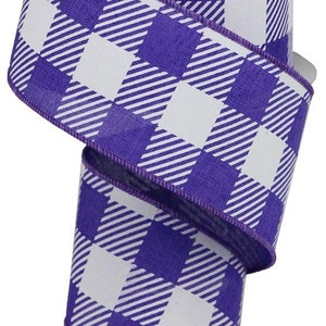 May include: A roll of purple and white buffalo plaid ribbon. The ribbon has a white background with purple squares and white stripes.