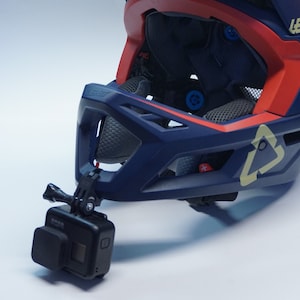 May include: A blue and red full-face helmet with a visor and a GoPro camera attached to the front. The helmet has the word "LEATT" printed on the side.