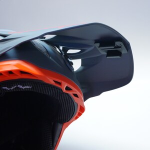 May include: A close-up of a black and orange full-face motorcycle helmet with a visor. The helmet has a built-in camera mount on the visor.