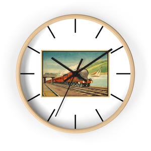 May include: Round wall clock with a light wood frame and black hands. The clock face features a vintage illustration of a red train on tracks, with a bridge and a sailboat in the background. The clock has black hour markers.