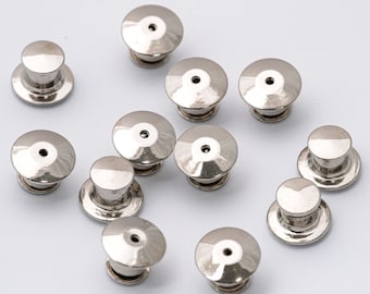 Op de afbeelding: Een close-up van elf zilveren metalen pinruggen. De pinruggen zijn rond en hebben een klein gaatje in het midden. Ze zijn willekeurig gerangschikt op een wit oppervlak.