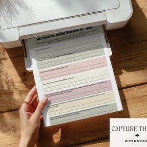 May include: A printed worksheet titled Worksheet for Anxiety Reduction in 7 Steps, featuring seven distinct sections with horizontal lines for writing, color-coded in soft pastel shades of green, pink, and beige, emerging from a white printer.
