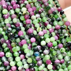 Op de afbeelding: Close-up van meerdere strengen kleine, gefacetteerde kralen. De kralen zijn een mix van groen, paars en zwart. Ze zijn strak aan elkaar geregen. Deze kralen zijn waarschijnlijk edelstenen, ideaal voor het maken van sieraden.