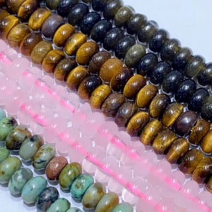 May include: Close-up of several strands of beads in various colors. The beads include shades of brown, black, pink, and turquoise. The beads are strung on pink and white string, and are likely for jewelry making.