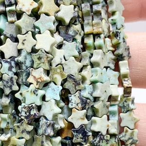 May include: Close-up of star-shaped beads in green, brown, and grey hues. The beads have a natural, textured finish, with colour and pattern variations. These beads are suitable for jewellery making.
