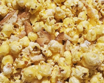 May include: A close-up of a bowl of popcorn with a buttery, yellow color. The popcorn is mixed with small, crispy, brown pieces of bread.