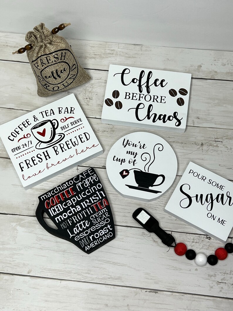 May include: A collection of coffee-themed wooden signs with black and white lettering. The signs feature phrases like "Coffee & Tea Bar", "Coffee Before Chaos", "You're My Cup Of", and "Pour Some Sugar On Me". There is also a small burlap bag with the words "Fresh Coffee" printed on it.