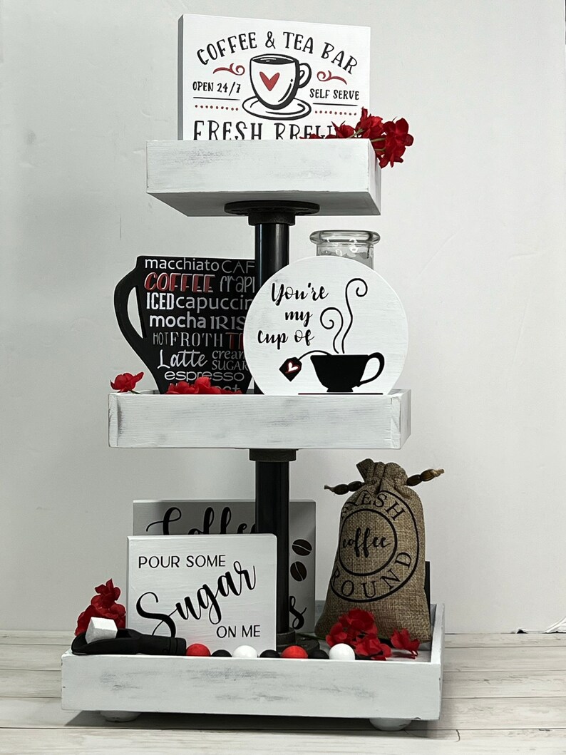 May include: A white tiered tray with three levels, decorated with coffee-themed signs and accessories. The top level has a sign that reads "Coffee & Tea Bar, Open 24/7, Self Serve, Fresh Brewed". The middle level has a sign that reads "You're my cup of" with a coffee cup and steam design. The bottom level has a sign that reads "Pour some Sugar on me" and a burlap bag with the words "Fresh Coffee Ground".