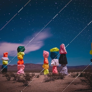 Puede incluir: Una colección de rocas apiladas y coloridas bajo un cielo estrellado. Las rocas están pintadas en varios tonos de rosa, verde, amarillo, azul y naranja. Las rocas están dispuestas en línea, con cada pila de diferente altura.