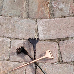 May include: Three back scratchers made of metal. One is black, one is copper, and one is a twisted black metal.