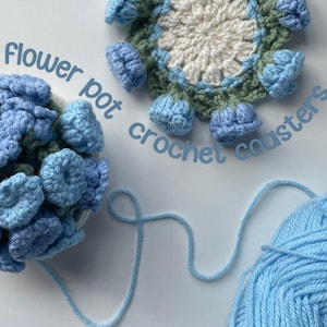 May include: Crocheted flower pot coasters in shades of blue, green, and white. The coasters are round with a flower design and the text "Flower pot crochet coasters". A ball of light blue yarn is in the image.