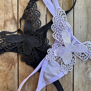 May include: Two pairs of lingerie with butterfly lace detailing. One pair is black and the other is lavender.