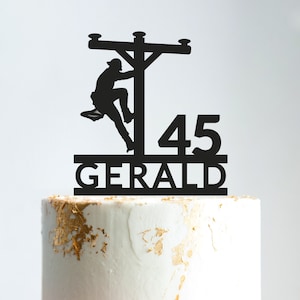Op de afbeelding: Zwarte silhouet caketopper van een persoon die een elektriciteitspaal beklimt met het nummer 45 en de naam GERALD eronder.