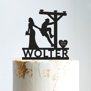 Op de afbeelding: Zwarte silhouet-taarttopper van een bruid en bruidegom. De bruidegom klimt op een elektriciteitspaal. De bruid houdt een boeket bloemen vast. De topper bevat de tekst "WOLTER" en "28.09.2023".