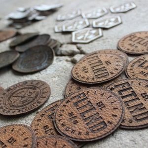 May include: Close-up of several round, brown leather patches with the text "Flatland Est. 2018 Metal Works" engraved on them.