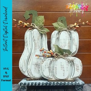 Puede incluir: Tres calabazas de madera blancas con detalles desgastados, dispuestas sobre un soporte decorativo. Cada calabaza tiene un tallo verde, hojas artificiales y pequeñas bayas naranjas. La imagen incluye el texto "Instant Digital Download" y "SVG & DXF Format".