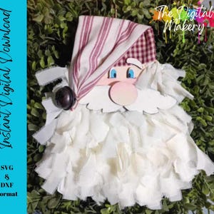 May include: A white, fluffy beard with a red and white striped hat and a white face with blue eyes. The face has a pink nose and a white moustache. The beard is made of fabric and is a craft project.