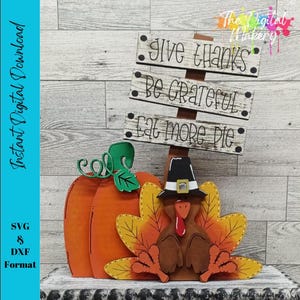 May include: A decorative Thanksgiving sign featuring a wooden post with three horizontal planks reading Give Thanks, Be Grateful, and Eat More Pie. An orange pumpkin with a green stem and a brown turkey wearing a black pilgrim hat are at the base.
