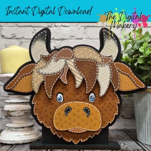 Pode incluir: Uma cabeça de vaca Highland em camadas, marrom e bege, com olhos azuis e detalhes costurados. A vaca tem chifres grandes e uma juba desgrenhada. O texto diz "Instant Digital Download" e "The Digital Makery".