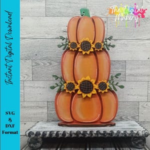 May include: A wooden pumpkin decoration with three stacked pumpkins, adorned with sunflowers and green leaves. The pumpkins are orange with a green stem. The text "Instant Digital Download" is on the left side of the image. The Digital Makery logo is in the top right.
