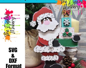 May include: A wooden Santa Claus figure with a red suit, white beard, and black boots. The figure is holding a stack of decorative blocks. The image includes the text "Instant Digital Download" and "SVG & DXF Format".