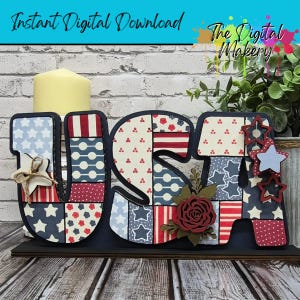 May include: A patriotic USA sign with a candle, featuring red, white, and blue patterns. The letters are decorated with stars, stripes, and floral accents. The sign is on a dark wooden base.