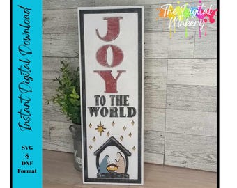 Könnte beinhalten: Ein weißes Holzschild mit den Worten "JOY TO THE WORLD" in schwarzer Schrift. Das Wort "JOY" ist rot und hat einen verwitterten Look. Das Schild zeigt auch eine Krippe mit einem Stern über dem Stall.