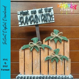 Puede incluir: Decoración de calabazas de madera con tres calabazas y un letrero que dice "Meet me at the Pumpkin Patch". Las calabazas son naranjas con tapas verdes y lazos de cuerda. El letrero es blanco con letras negras. El fondo es una pared de madera.