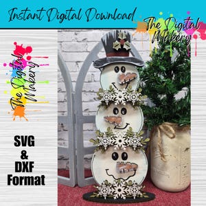 Puede incluir: Decoración de muñeco de nieve de madera con tres secciones apiladas, cada una con una cara sonriente, una nariz de zanahoria y detalles de copos de nieve. El muñeco de nieve lleva un sombrero de copa y está sobre una base negra. El texto "Instant Digital Download" está en la parte superior.