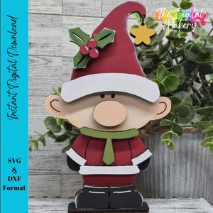 May include: A wooden Christmas gnome decoration with a red hat, coat, and black boots. The gnome has a white beard, a round nose, and a green scarf. The hat is adorned with holly and berries. The text "Instant Digital Download" is on the left.