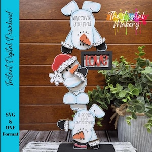 以下が含まれることがあります： 「Wherever you find」と「It feels like Christmas」の文字が入った、積み重ねられた雪だるまの装飾品。 雪だるまは人参の鼻、黒い手袋、赤いサンタ帽子をしています。 中央には「Love」の文字があります。